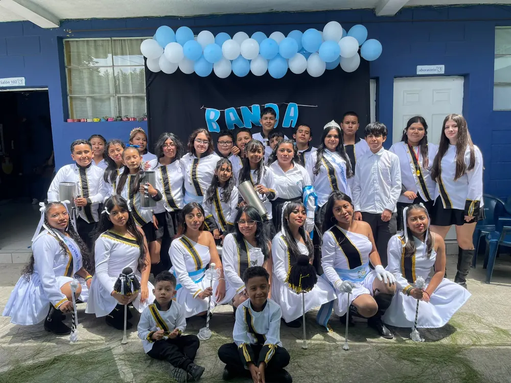 Integrantes de la banda del colegio posan con uniformes blancos y negros bajo un arco de globos celestes y blancos