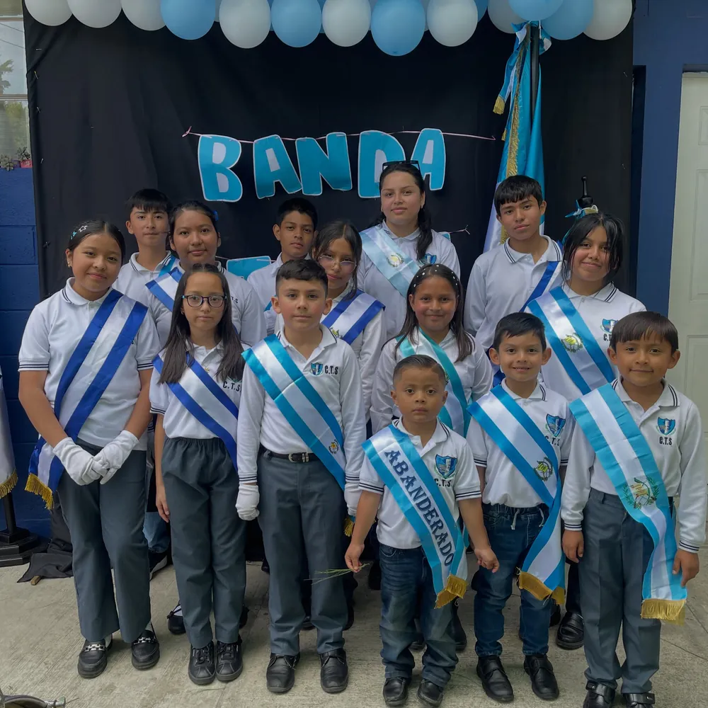 Estudiantes de la banda con uniforme y bandas celestes y blancas, frente a un letrero que dice Banda